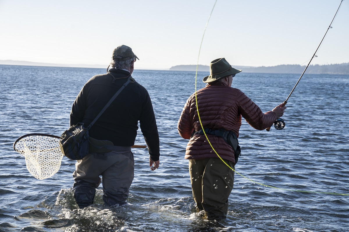 A guide advises his client while fly fishing in salt water for searun coastal cutthroat trout and salmon in northwest Washington State,