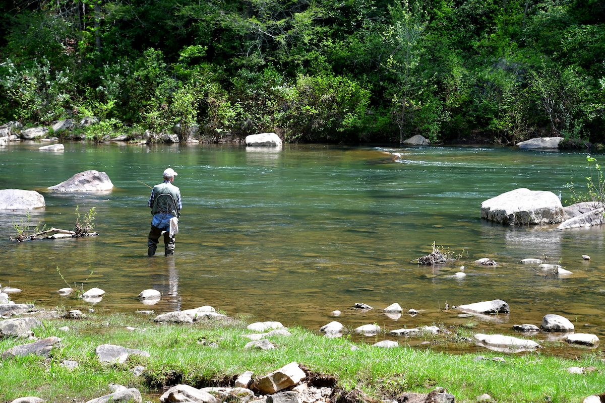 A fly angler in waders stands in the river with his line cast