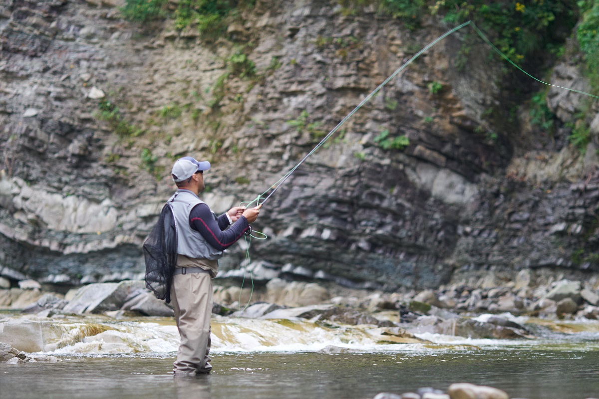 Mature man fly fishing in mountain river during summer day