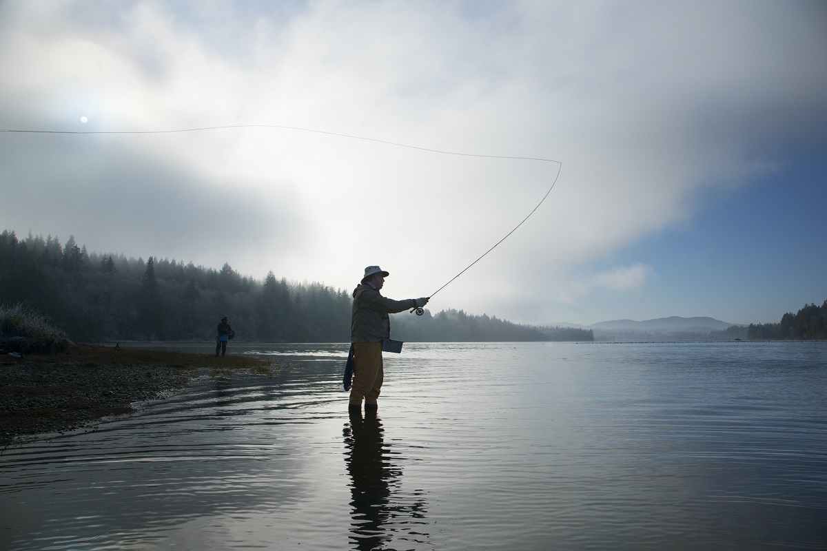 Silhouette of fisherman fly fishing for salmon and sea run cutthroat trout in Puget Sound near Olympia, Washington USA.